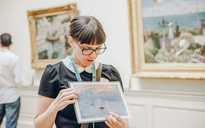 Tour guide at the Metropolitan Museum of Art holding a painting print in a gallery.