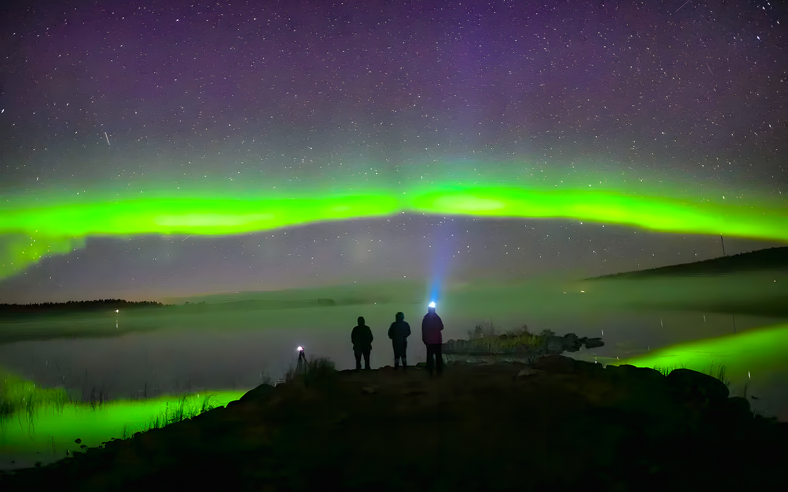 Travelers watching northern lights over snowy Rovaniemi landscape.