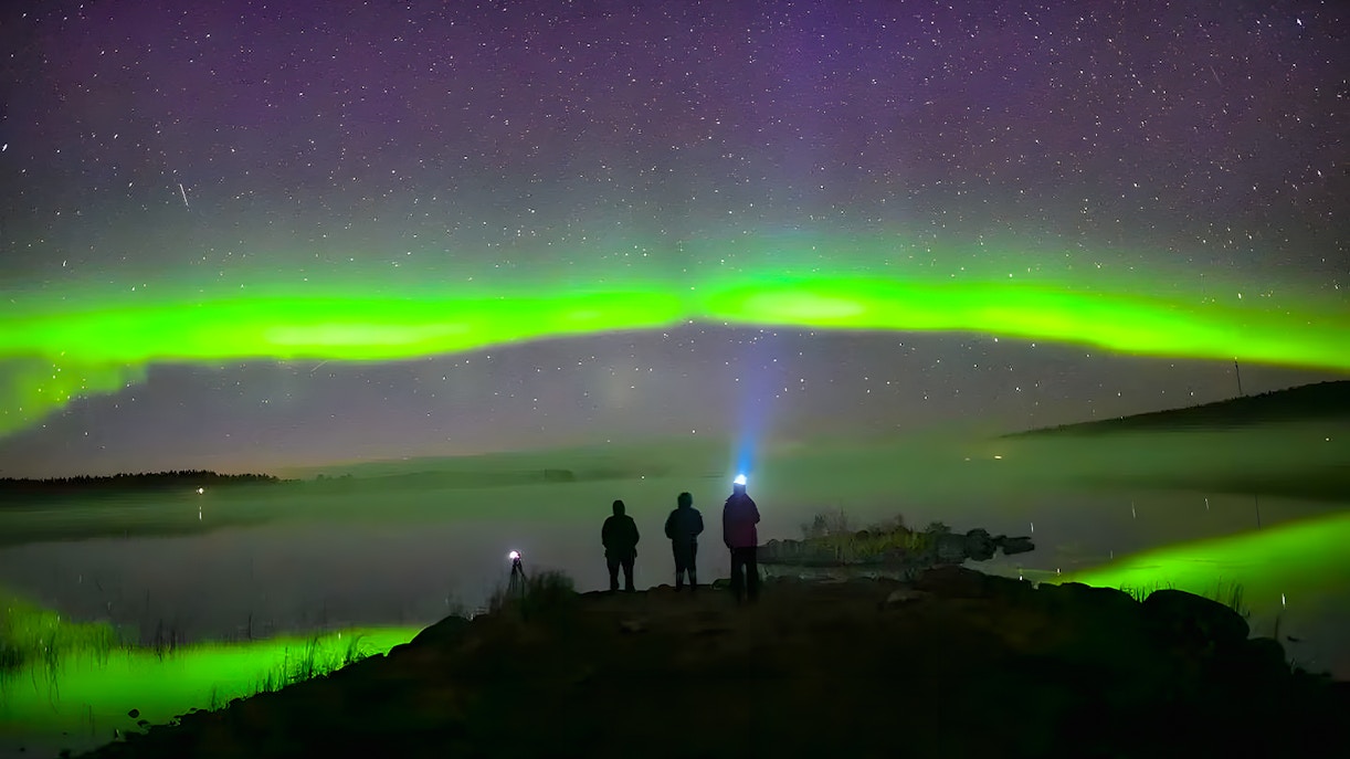 Northern lights over snowy landscape with travelers using head lamp