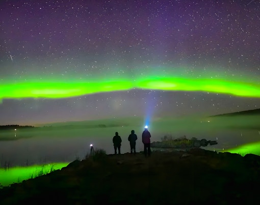 Travelers watching northern lights over snowy Rovaniemi landscape.