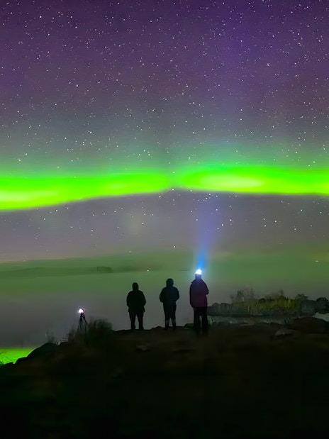 Travelers watching northern lights over snowy Rovaniemi landscape.