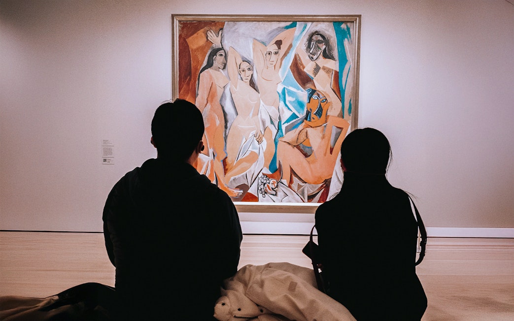 Visitors viewing Picasso's Les Demoiselles d'Avignon painting in a museum.