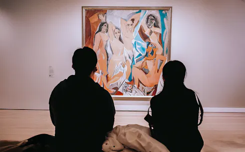 Visitors viewing Picasso's Les Demoiselles d'Avignon painting in a museum.