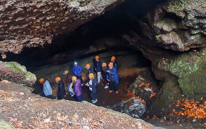 Group exploring a cave on Mount Etna tour, wearing helmets and jackets.