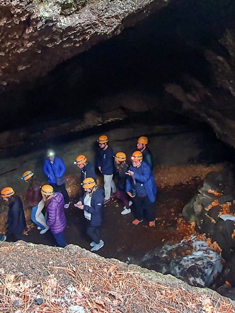 Group exploring a cave on Mount Etna tour, wearing helmets and jackets.