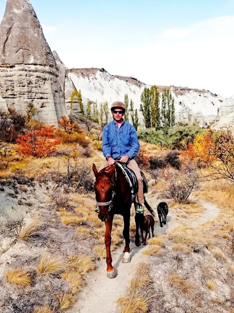 Horseback rider on a trail through Cappadocia's unique rock formations at sunset.