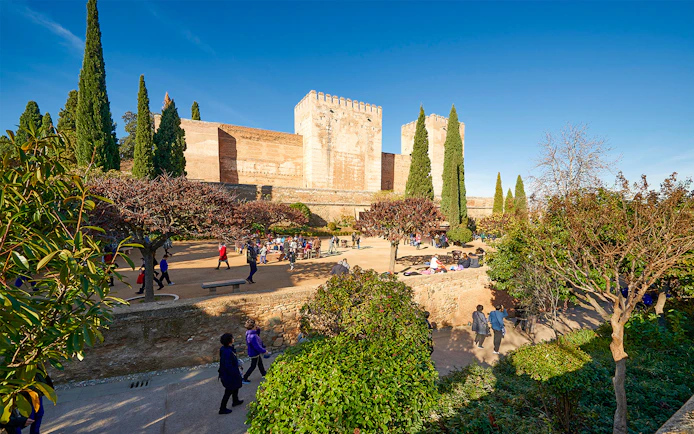 Visitors exploring Alhambra gardens with fortress walls in Granada, Spain.