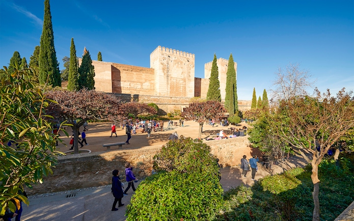 Visitors exploring Alhambra gardens with fortress walls in Granada, Spain.