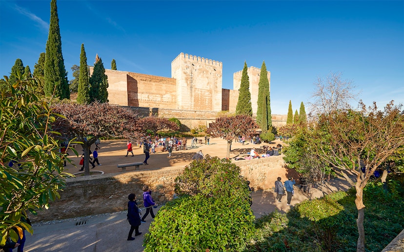 Visitors exploring Alhambra gardens with fortress walls in Granada, Spain.