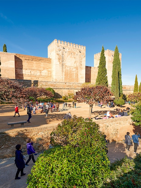 Visitors exploring Alhambra gardens with fortress walls in Granada, Spain.