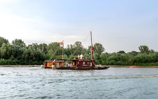 Tourists on a traditional Galar cruise boat on the Vistula River, surrounded by lush greenery.