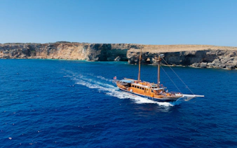 Cruise ship sailing near rocky coastline on Fernandes Gozo & Comino all-inclusive tour.