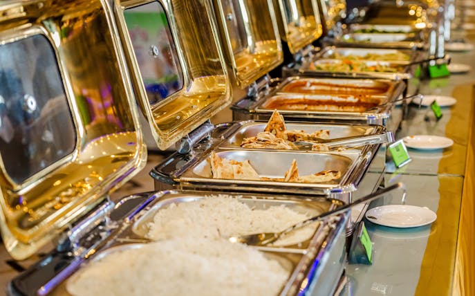 Indian buffet with rice, naan, and curry dishes in stainless steel trays.