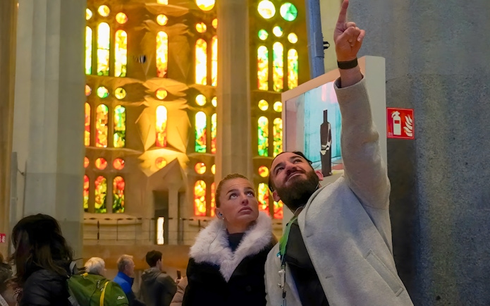 Guide explaining stained glass windows to tourist inside Sagrada Familia, Barcelona.