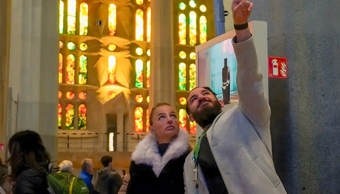 Guide explaining stained glass windows to tourist inside Sagrada Familia, Barcelona.