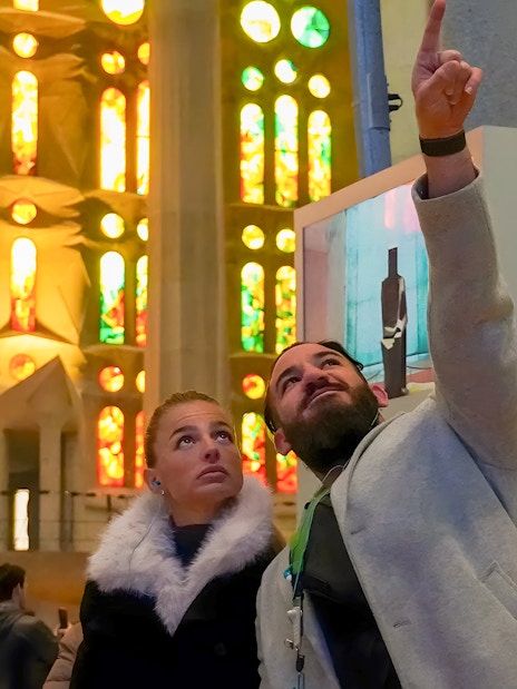 Guide explaining stained glass windows to tourist inside Sagrada Familia, Barcelona.