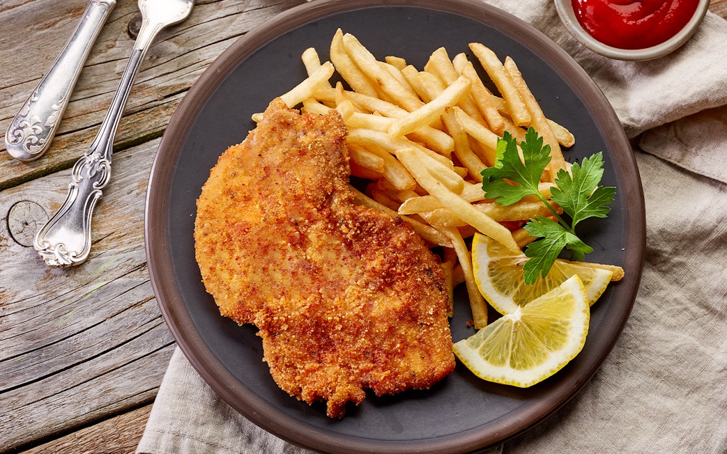 Viennese schnitzel with fries and lemon slices on a plate, Danube Canal cruise option.