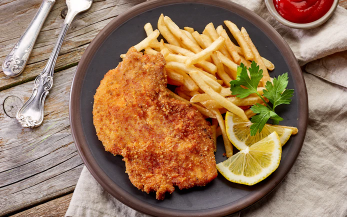 Viennese schnitzel with fries and lemon slices on a plate, Danube Canal cruise option.