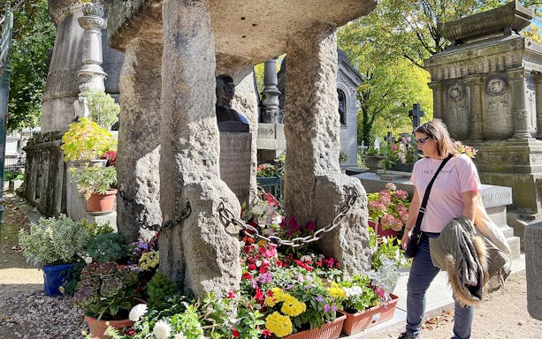 Visitor exploring a grave adorned with flowers at Père Lachaise Cemetery in Paris.