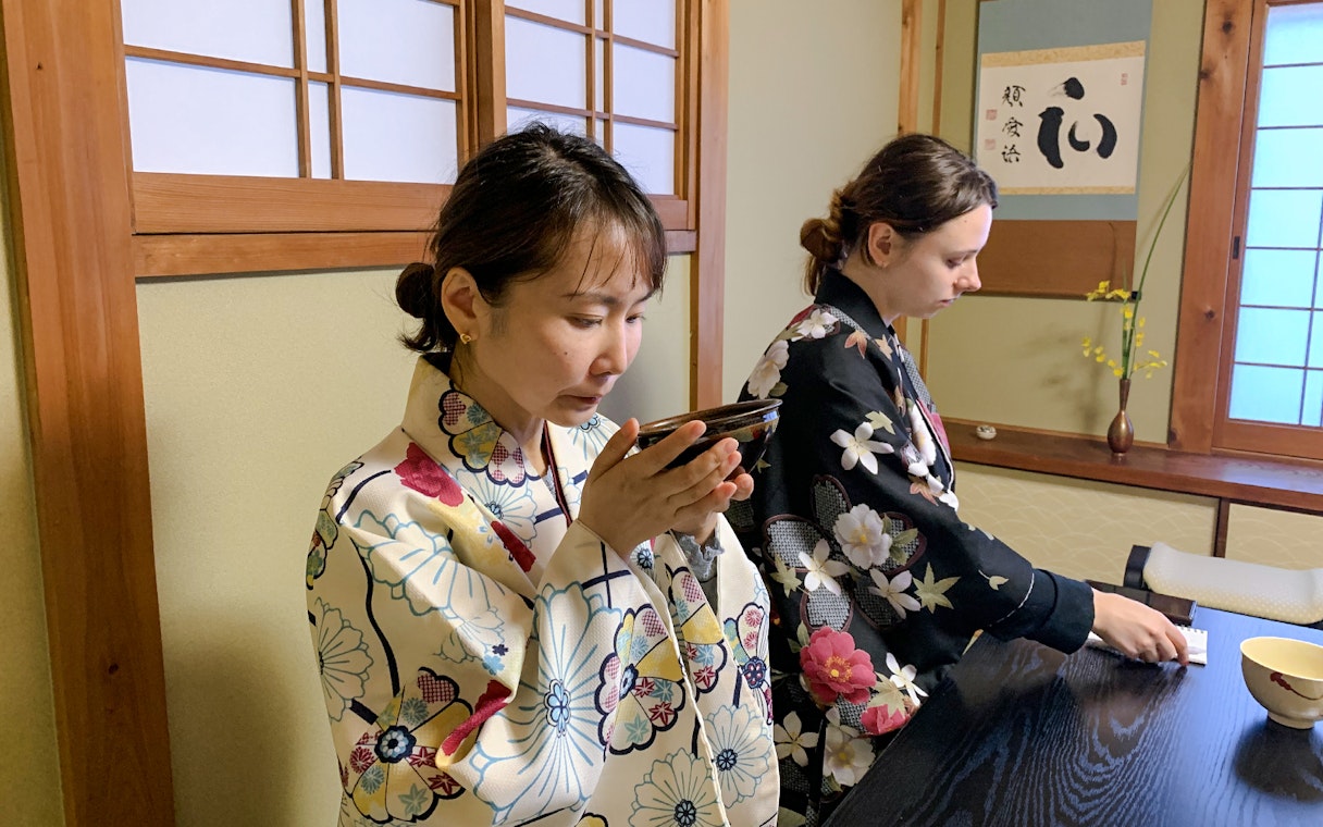 People participating in a traditional tea ceremony in Kyoto, wearing floral kimonos.