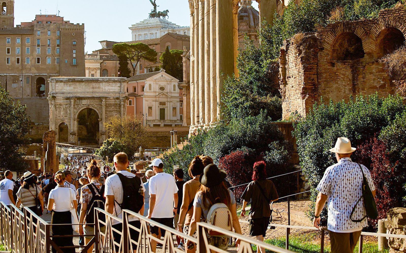 Tourists walking towards Palatine Hill in Rome, passing ancient ruins and the Arch of Titus.