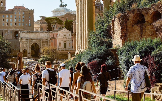 Tourists walking towards Palatine Hill in Rome, passing ancient ruins and the Arch of Titus.