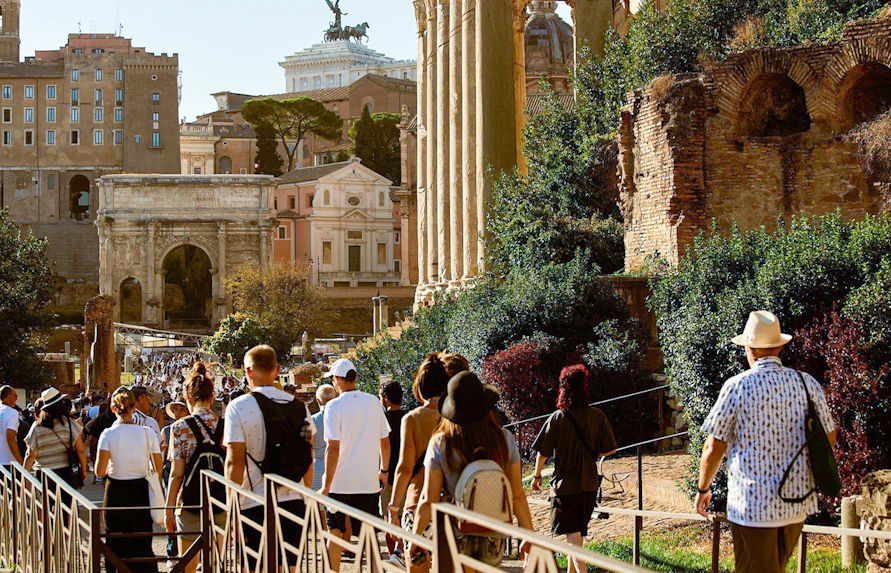 Tourists walking towards Palatine Hill in Rome, passing ancient ruins and the Arch of Titus.