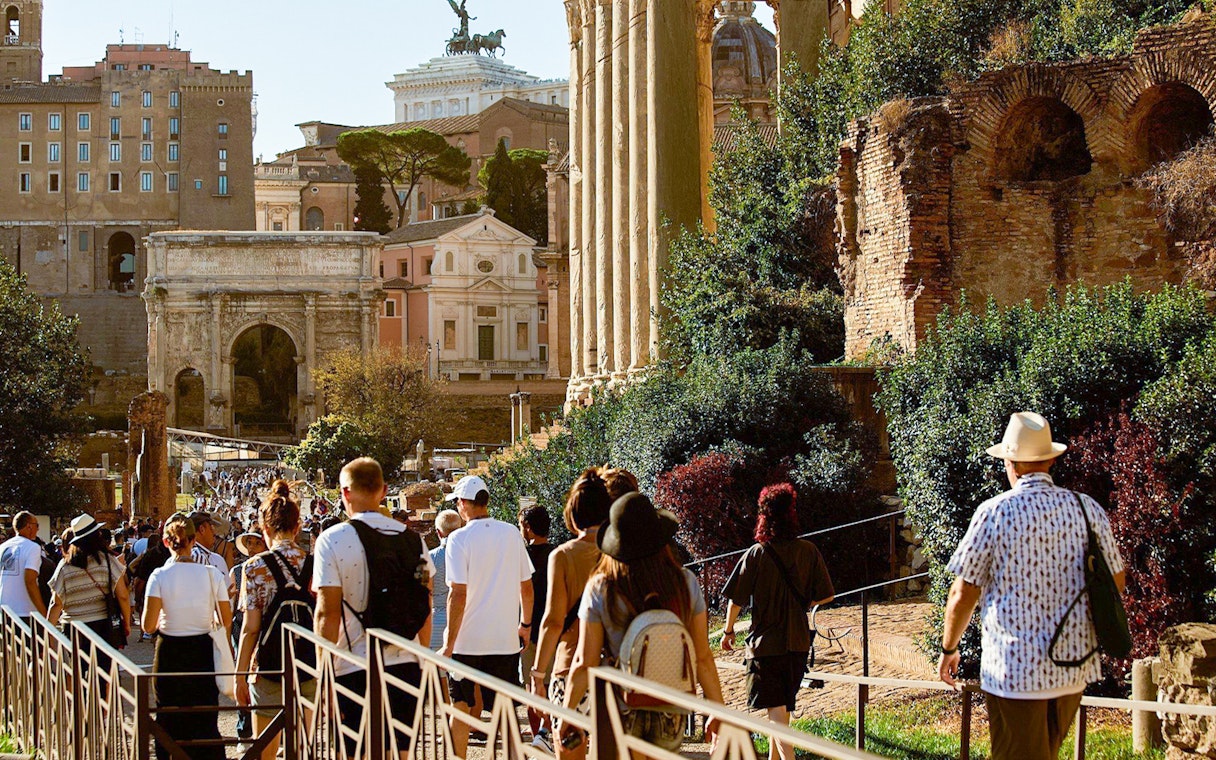 Tourists walking towards Palatine Hill in Rome, passing ancient ruins and the Arch of Titus.