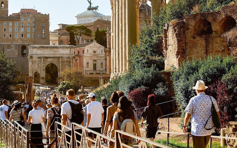 Tourists walking towards Palatine Hill in Rome, passing ancient ruins and the Arch of Titus.