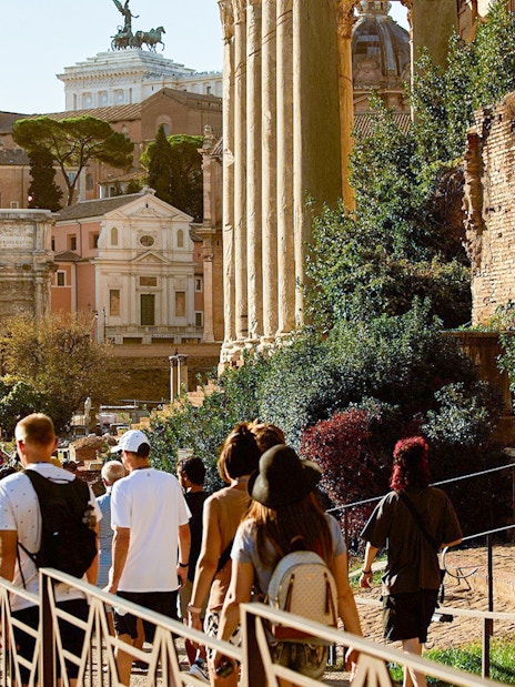 Tourists walking towards Palatine Hill in Rome, passing ancient ruins and the Arch of Titus.