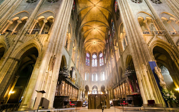 Interior view of Notre-Dame Cathedral in Paris with stained glass windows and vaulted ceilings.