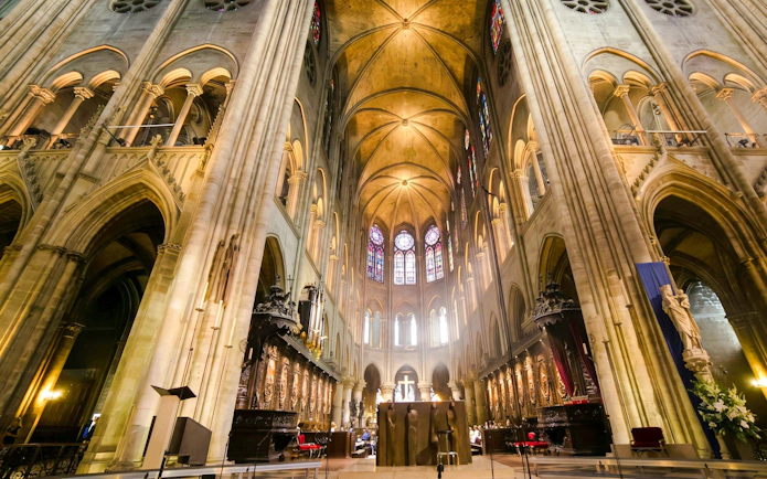 Interior view of Notre-Dame Cathedral in Paris with stained glass windows and vaulted ceilings.