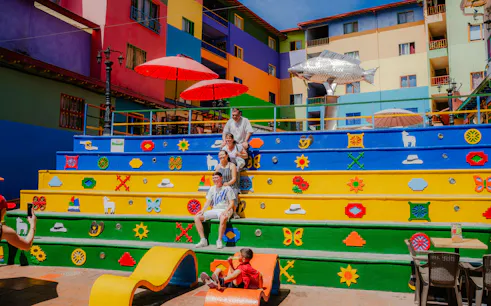 Colorful stairs at Plazoleta de los Zócalos, Guatapé, Colombia, with vibrant murals and people sitting.