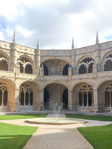 Jerónimos Monastery courtyard with ornate arches and central fountain in Lisbon, Portugal.