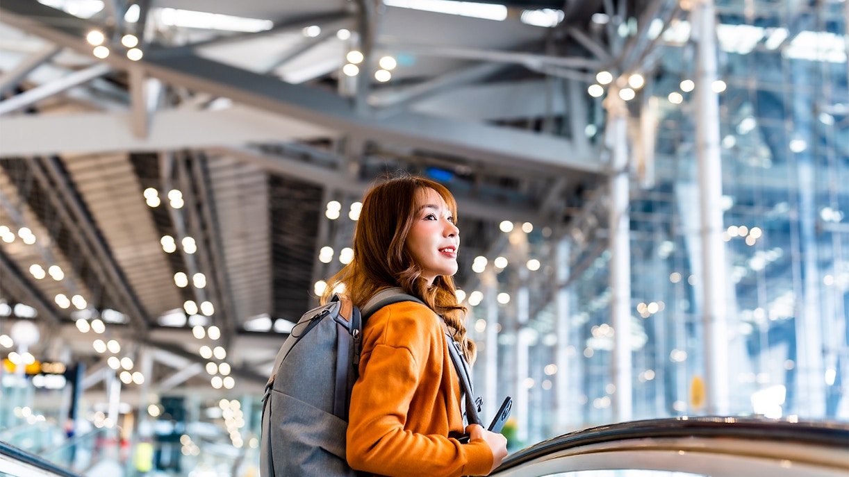 Traveler with backpack on escalator at a modern train station, using JR West Pass.