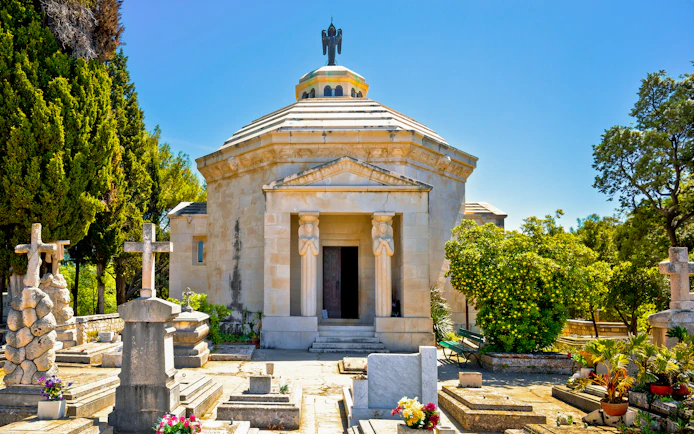Racic Mausoleum in Cavtat graveyard surrounded by tombstones and greenery.