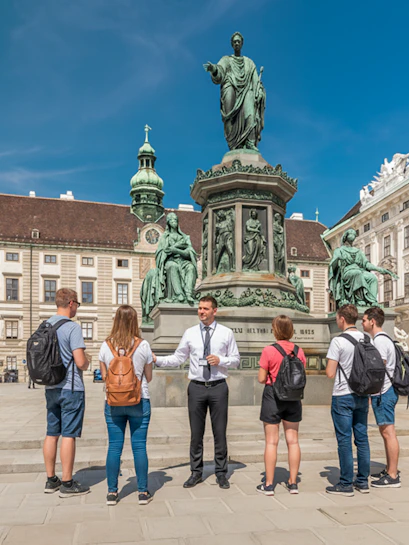 Tour guide explaining to guests in front of a statue at Hofburg Palace, Vienna.