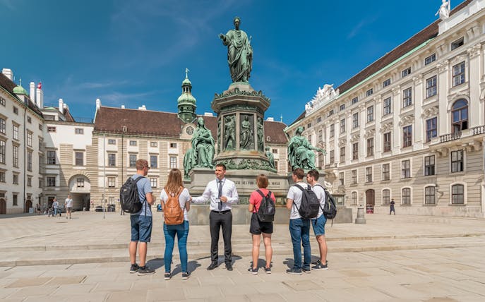 Tour guide explaining to guests in front of a statue at Hofburg Palace, Vienna.