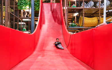 Child enjoying a ride down a large red slide in an indoor play area.