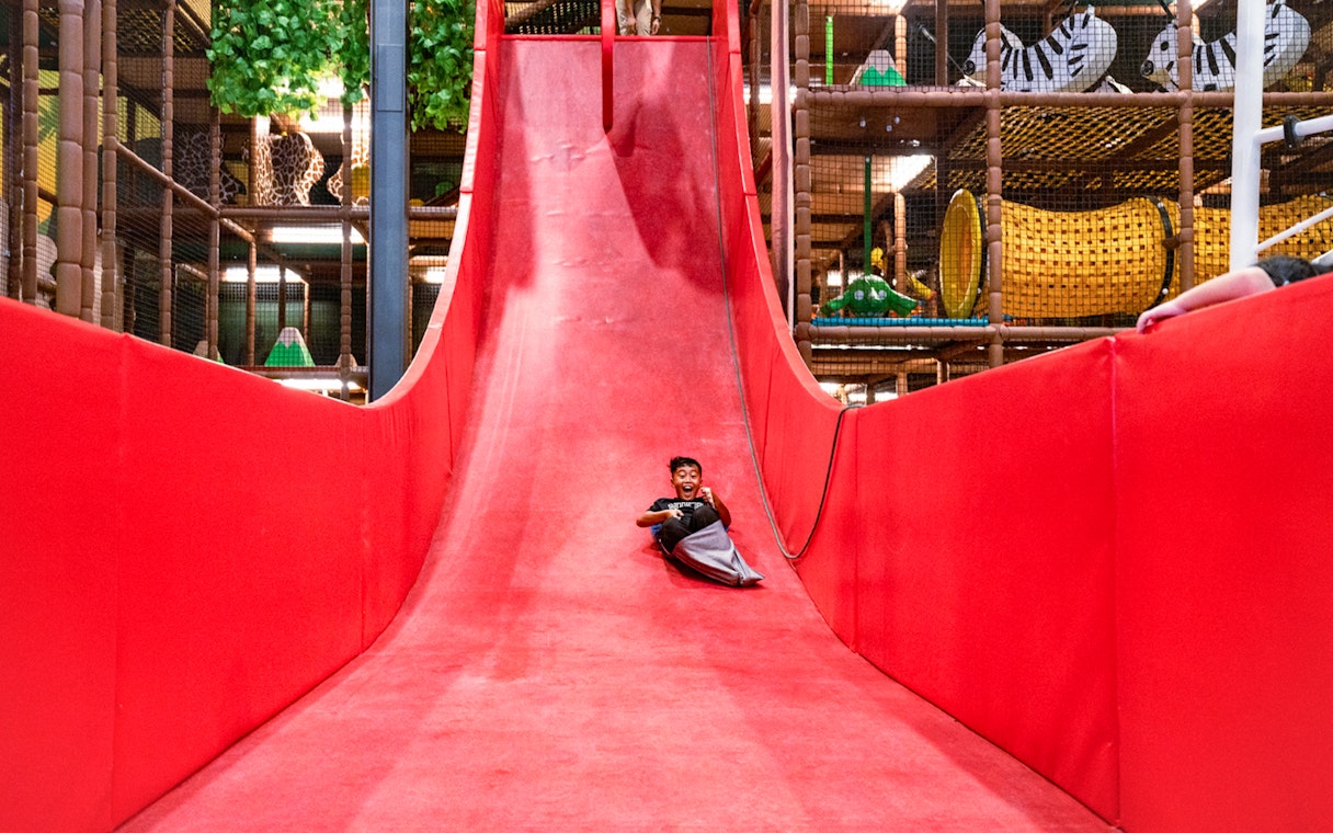 Child enjoying a ride down a large red slide in an indoor play area.