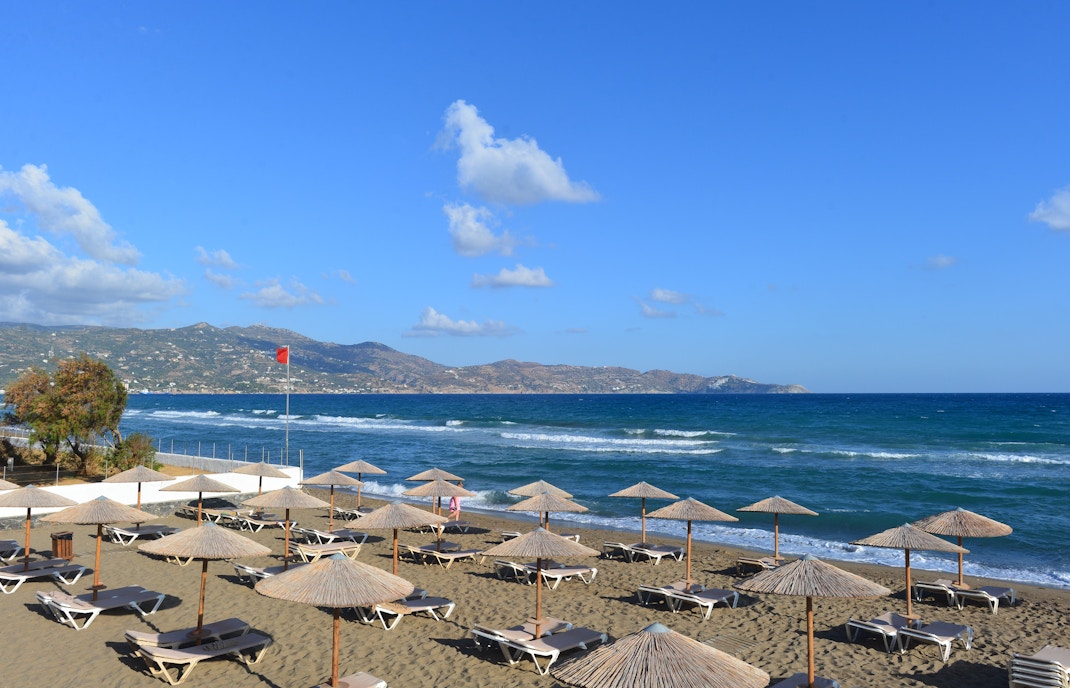 Sun loungers and umbrellas on Ammoudara Beach with mountains in the background.