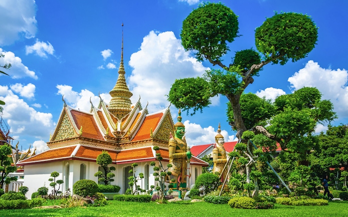 Grand Palace in Bangkok with ornate spire, guardian statues, and lush gardens.
