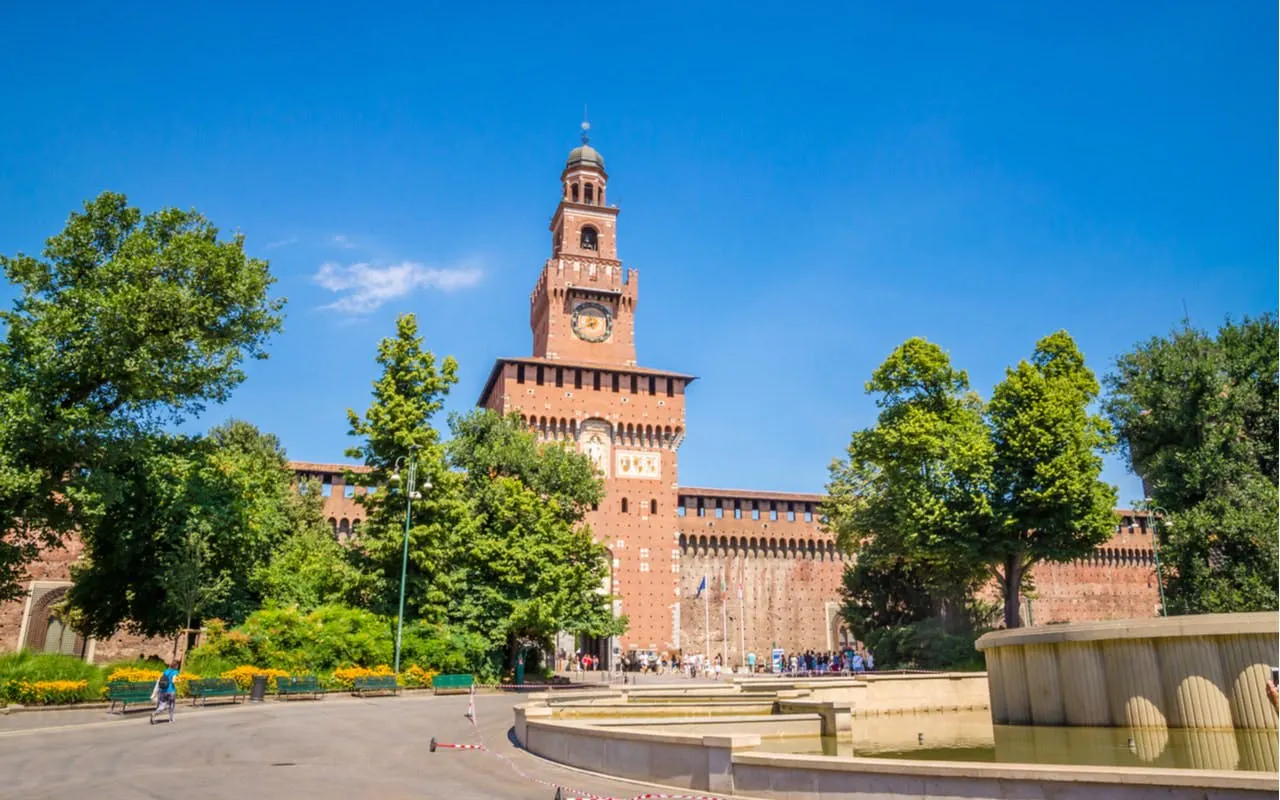 Sforza Castle in Milan, Italy, surrounded by trees and a fountain, part of a self-guided city exploration game.