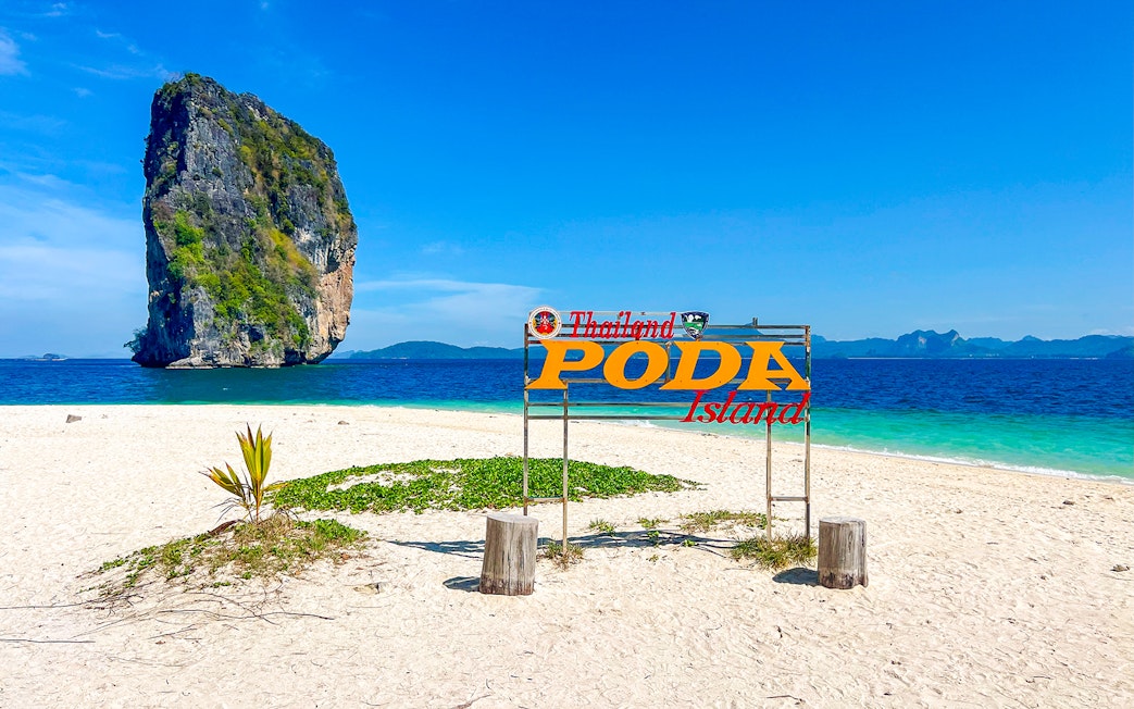 Poda Island sign on sandy beach with limestone rock in Thailand.