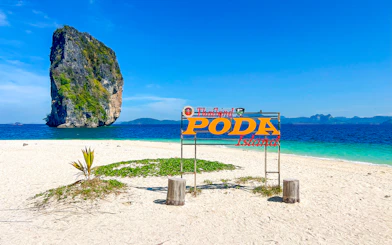 Poda Island sign on sandy beach with limestone rock in Thailand.