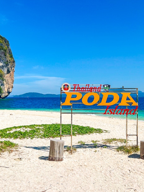 Poda Island sign on sandy beach with limestone rock in Thailand.