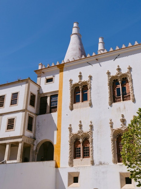 National Palace of Sintra with ornate windows and conical chimneys under a clear blue sky.