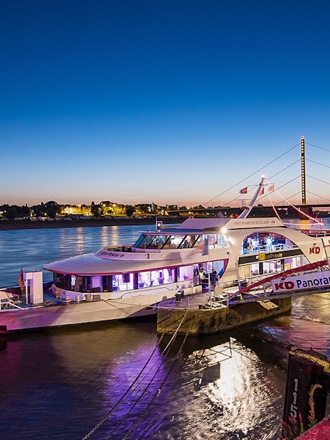 Cruise boat docked on the Rhine River at sunset in Düsseldorf, Germany.