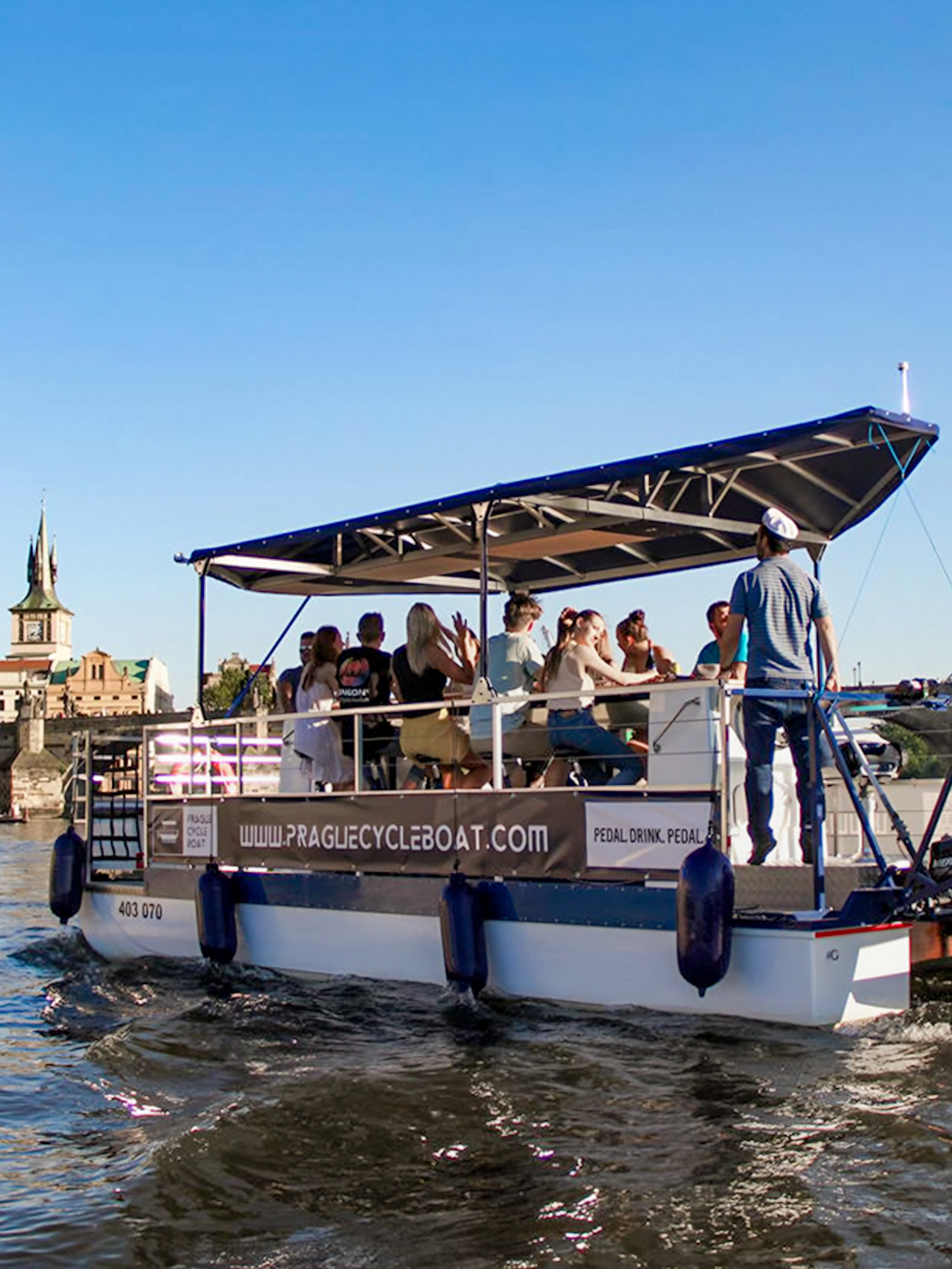 Cycle boat on Vltava River near Charles Bridge, Prague, with passengers enjoying unlimited beer.