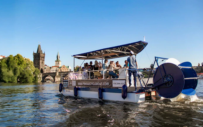 Cycle boat on Vltava River near Charles Bridge, Prague, with passengers enjoying unlimited beer.
